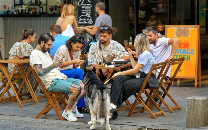 People having drinks on sidewalk with dog on leash